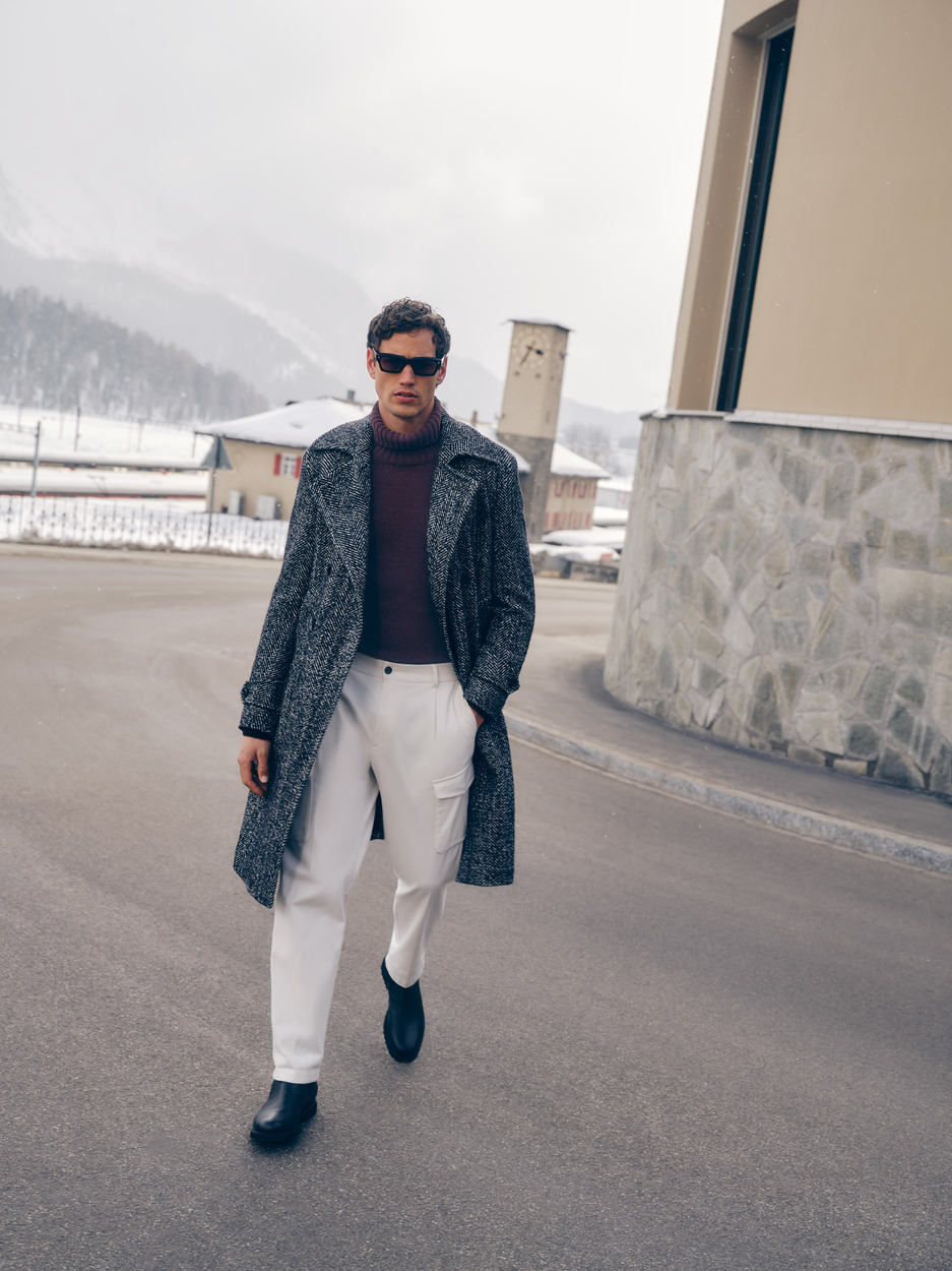 a man wearing sunglasses and a long coat walking down a street