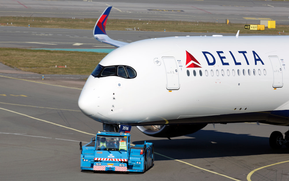 Detalle del morro de un A350 de Delta en tierra con un tractor de retroceso conectado a su tren delantero