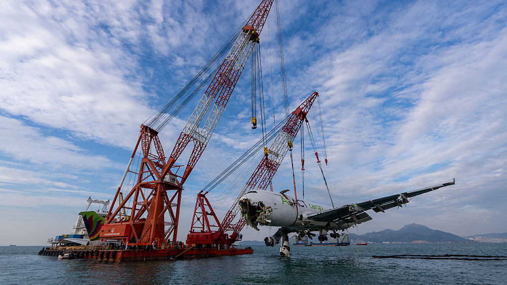 El fuselaje sin la cola colgando de una grúa que lo va a depositar en una barcaza