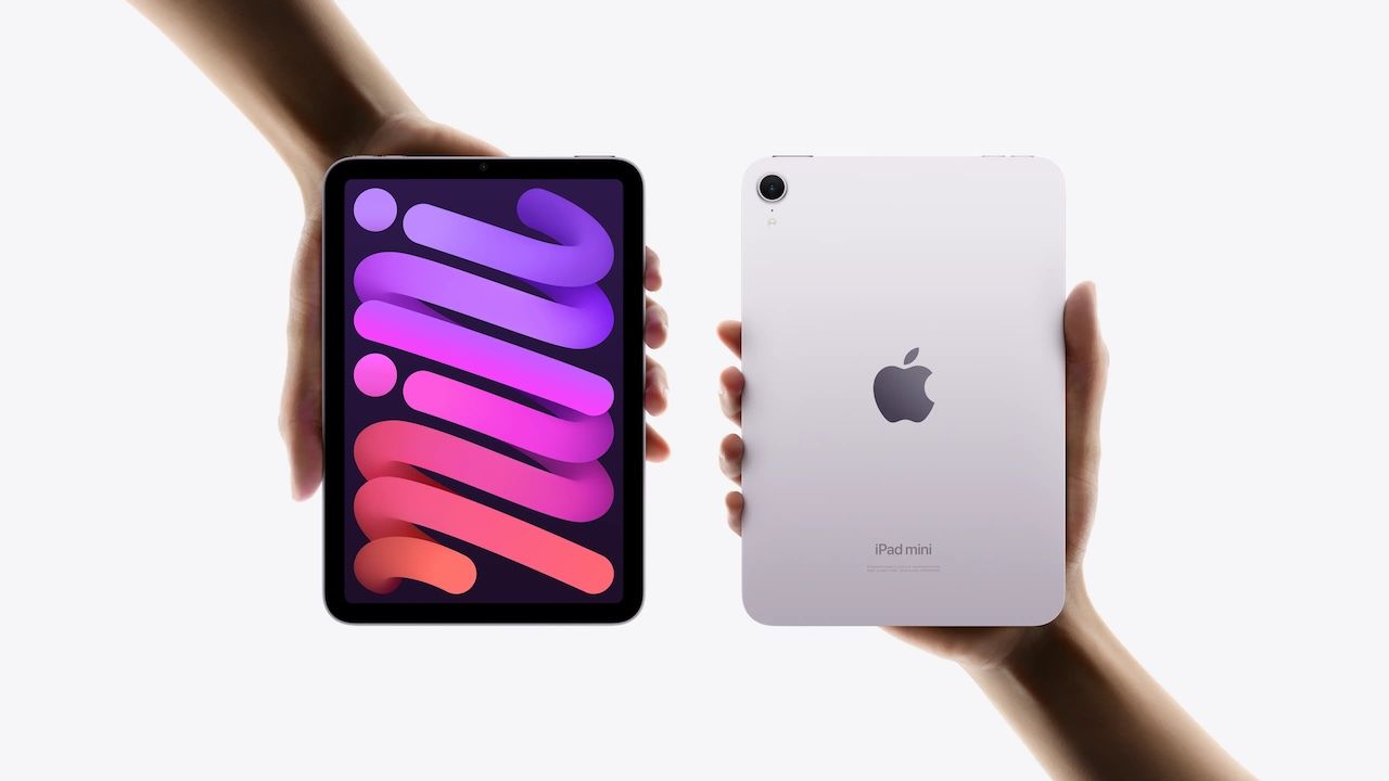 Dos manos sujetan verticalmente un iPad mini, mostrando a la izquierda la pantalla frontal encendida con un fondo degrade púrpura y a la derecha su parte trasera en color malva con el logotipo de Apple.